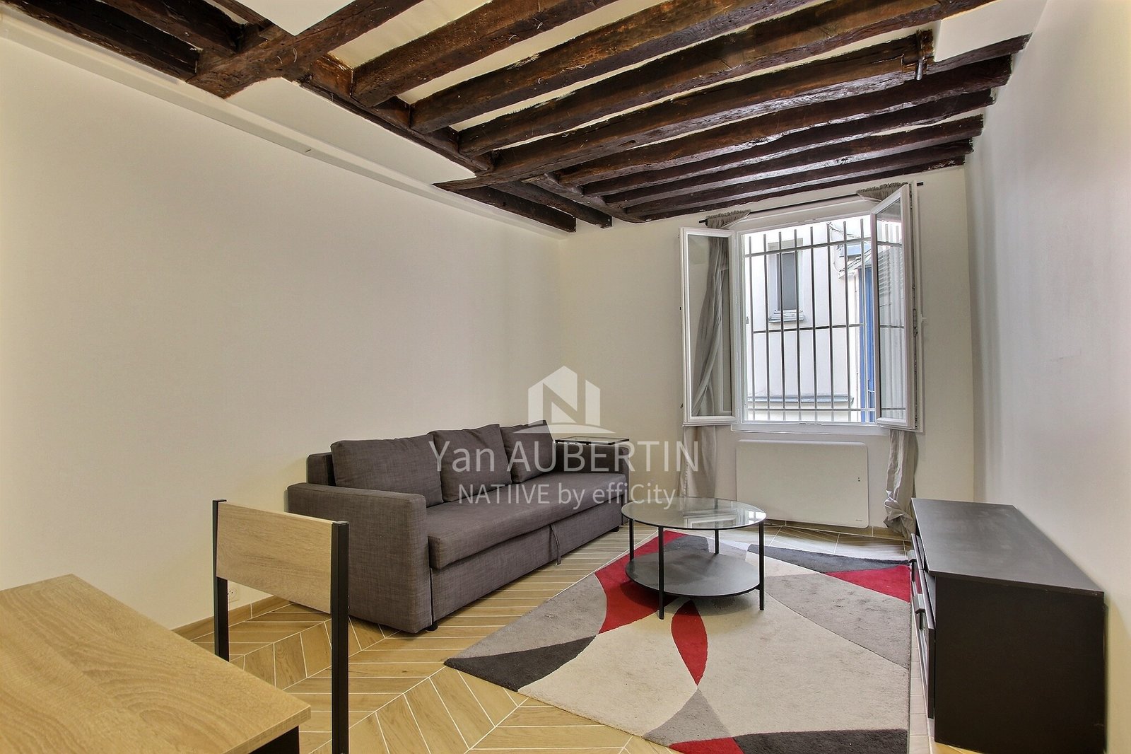 Pièce de vie du studio à Saint-Germain-des-Prés, avec poutres apparentes et fenêtre sur cour.